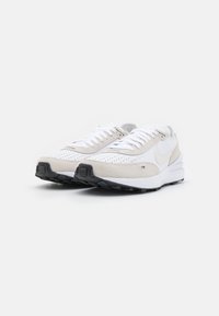 Nike tenisice s gornjim dijelom od bijele mrežice i bež nubuk detaljima. Imaju perforirani dizajn, bijele vezice i crnu gumenu potplatu.