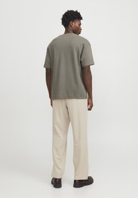 Olivově zelené bavlněné tričko s krátkým rukávem, kombinované se světle béžovými kalhotami a tmavě hnědými botami, viděné ze zadní strany.