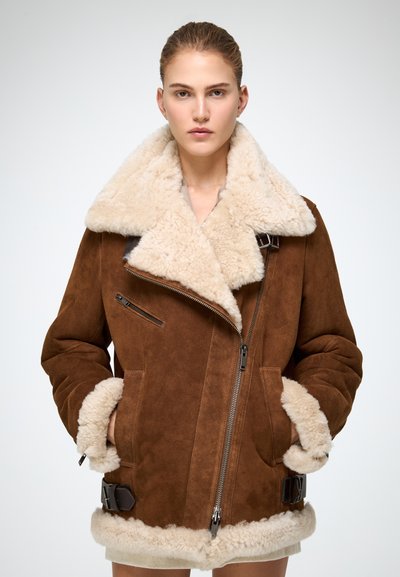 Braune Wildlederjacke mit einem flauschigen, cremigen Lammfellkragen und -manschetten, ausgestattet mit einem Reißverschluss vorne, seitlichen Taschen und verstellbaren Schnallen am Saum.