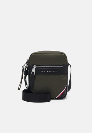 Small olive green crossbody bag with black adjustable strap, zipper pocket, and Tommy Hilfiger logo on front panel.