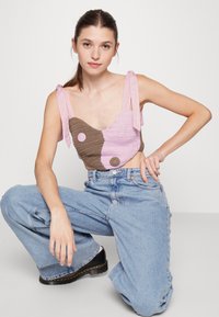 Top de crochê cropped com secções em rosa e castanho, apresentando um decote redondo e alças de laço. Combinado com jeans de cintura alta.