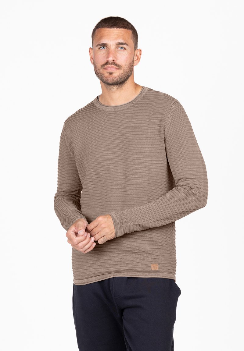 Langarm-T-Shirt mit Rundhalsausschnitt aus strukturiertem braunem Stoff mit gerippten Mustern und einem kleinen Logopatch am Saum. Trägt man zu dunklen Hosen.