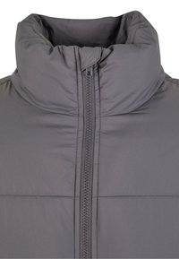 Graue Steppjacke mit hohem Kragen, durchgehendem Reißverschluss und horizontalen Nahttexturen. Das Material wirkt wasserabweisend und isoliert.