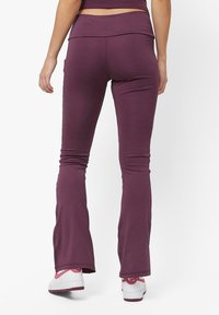Burgunderfargede slengbukser til yoga laget av elastisk stoff, med høy midje og en glatt tekstur, kombinert med hvite joggesko.