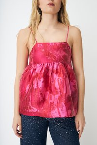 Kvinne iført en rød og rosa glitrende ermeløs topp med tynne stropper og mørkeblå jeans dekorert med små hvite perler.