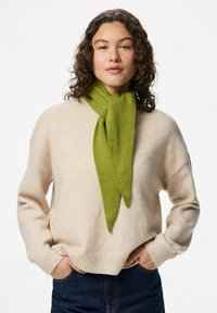 Bufanda verde drapeada alrededor del cuello, hecha de material suave; combinada con un suéter crema y jeans azul oscuro. Diseño sencillo sin patrones.