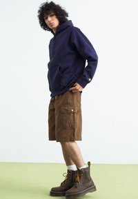 Marine hettegenser, brune cargo-shorts og brune snørebukser. Genseren har en kengurulomme; shortsene har store sidelommer.