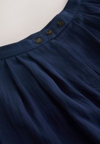 Jupe en velours côtelé bleu marine avec tissu froncé sous la taille et trois boutons foncés fermés au centre devant.