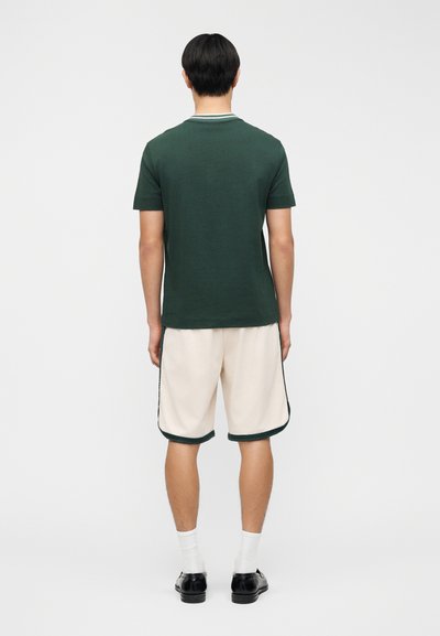 Πράσινο κοντομάνικο πουκάμισο με ριμπ γιακά, σε συνδυασμό με ανοιχτό μπεζ σορτς που έχει σκούρες πράσινες λεπτομέρειες στα πλαϊνά.