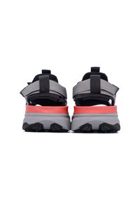 Scarpe da ginnastica grigie e nere con un accento rosso. Presentano cinturini regolabili e suole testurizzate per una migliore aderenza. La vista posteriore mostra un design stratificato.