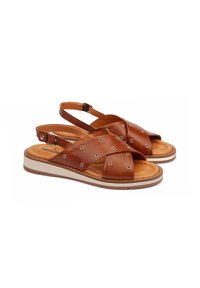 Sandalias de cuero marrón con correas cruzadas, ojales de metal decorativos y una suela beige. Cuenta con una correa ajustable en el tobillo para un mejor ajuste.