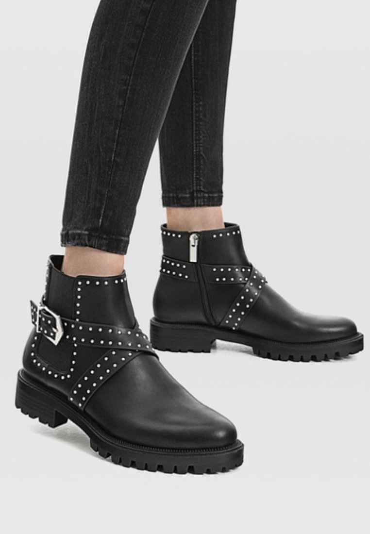 Bottes noires jusqu'à la cheville en cuir lisse, ornées de clous en argent et d'une large sangle avec une boucle. Semelle en caoutchouc crantée pour une meilleure adhérence.