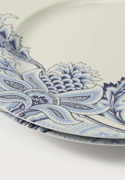 Assiettes en porcelaine blanche empilées, avec des motifs détaillés de fleurs et de feuilles bleues le long des bords sur un fond blanc.