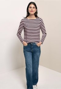 Långärmad randig topp i mörk burgundy och ljusrosa, kombinerad med vida blå jeans. Modellen står med händerna i fickorna och vänder sig framåt.