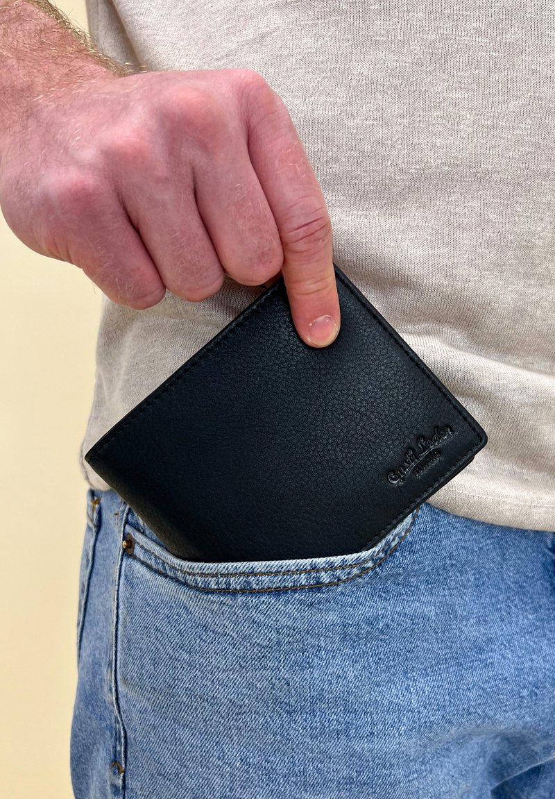 Black leather wallet partly in a jeans pocket, showcasing pebbled texture and a smooth edge. Logo embossed in the bottom right corner.