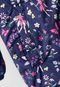 Jūrinės spalvos audinys su spalvingais gėlių ir drugelių raštais. Yra kišenės arba slotų detalė. Lygus tekstūra, pritaikytas dizainas.