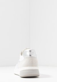 Białe sneakersy z perforowanymi panelami bocznymi, szarym zamszowym tyłem i błyszczącym srebrnym akcentem na pięcie. Posiadają gumową podeszwę dla lepszej przyczepności.