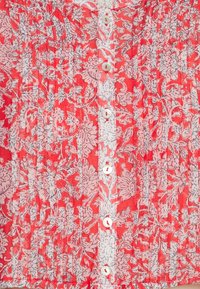 Tessuto a fiori rosso e bianco con pieghe verticali e una fila di piccoli bottoni bianchi al centro.