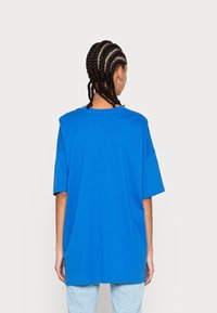 Blå överdimensionerad t-shirt i bomull med korta ärmar, rund hals och avslappnad passform. Slät textur, inga mönster eller detaljer synliga.