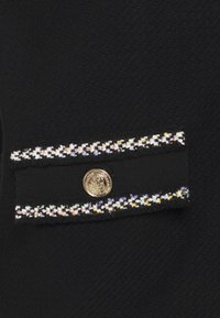 Černá látka s texturovanou tkaninou. Obsahuje dekorační lem s vícebarevnými nitěmi a zlatý knoflík na klopě.