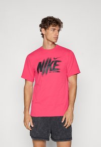 Lyserød bomulds T-shirt med et iøjnefaldende sort "NIKE" grafisk design med penselstrøg, rund hals og korte ærmer.