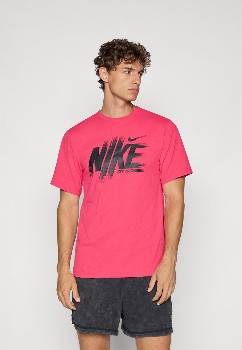 Lyserød bomulds T-shirt med et iøjnefaldende sort "NIKE" grafisk design med penselstrøg, rund hals og korte ærmer.
