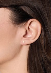 Złoty kolczyk w kształcie okrągłym, minimalistyczny wzór, mała średnica, gładka powierzchnia, umieszczony na małżowinie usznej, zbliżenie.