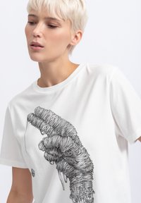 Witte katoenen t-shirt met een grafisch ontwerp van een hand, gemaakt van ingewikkelde, over elkaar heen lopende lijnen. Ronde hals en korte mouwen.