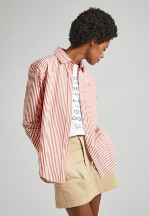 Maglietta a righe rosse e bianche con colletto a camicia, abbinata a una gonna beige con tasche a patta. Tessuto texture, vestibilità comoda.