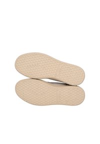 Semelles de chaussures avec une surface en caoutchouc beige texturée présentant un motif en nid d'abeille et un nom de marque en relief. La forme est plate et arrondie au niveau de l'orteil.