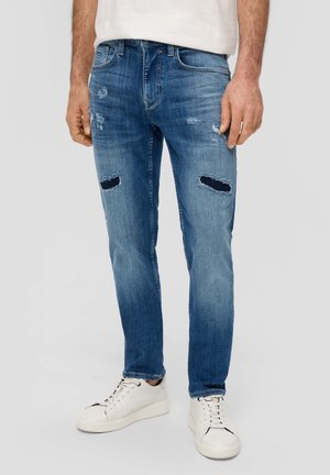 Jeans de denim desgastado en azul claro con detalles rasgados en las rodillas, de corte slim, y combinados con zapatillas blancas.