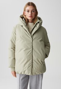 Giacca puffer verde chiaro con un grande cappuccio, zip frontale e dettagli a costine sui polsini. Presenta una texture liscia e lucida e una vestibilità ampia.