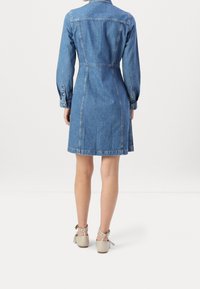 Vestito di jeans con maniche lunghe, vita aderente e forma a trapezio. Colore azzurro chiaro con dettagli di cucitura e polsini con bottoni.