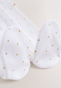 Pyjama bébé blanc avec pieds, avec de petits motifs d'étoiles dorées dispersés sur le tissu, présenté à plat sur un fond neutre.