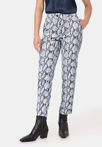Witte en navy slangenprint broek, tapered fit, met een platte voorkant, riemlussen en zijzakken, gecombineerd met zwarte enkelhoge laarzen.
