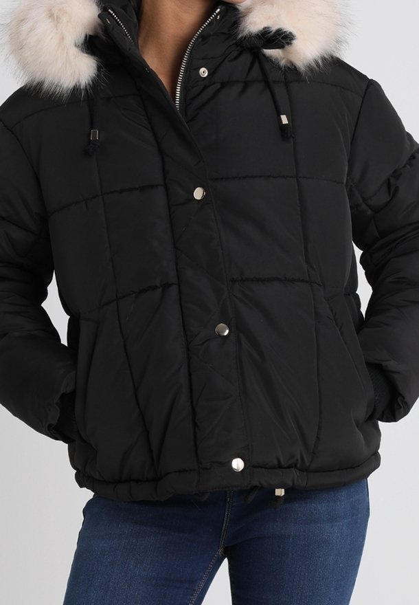 Svart quiltad jacka med pälsbeklädd luva, blixtlås framtill och tryckknappar, bärs med blå jeans.