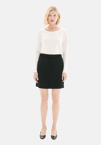 Un haut à manches longues blanc associé à une jupe noire taille haute avec une ceinture. La tenue est complétée par des escarpins noirs.