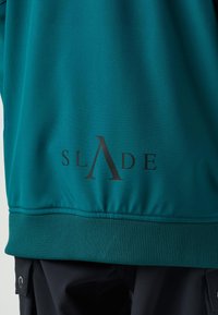 Felpa con cappuccio turchese con finitura texture, con il marchio "SLADE" stampato in nero sulla parte inferiore della schiena. Orlo e polsini a coste.