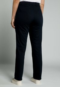 Pantalones negros con un diseño de pierna recta, hechos de una tela suave. Cintura elástica, detalles de costura mínimos, combinados con zapatos beige.
