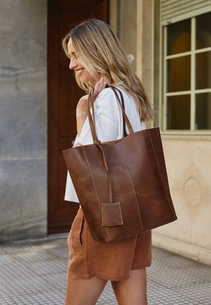 Braune Leder-Tote mit vertikaler Naht und einer kleinen aufgenähten Tasche. Sie hat lange Tragegriffe und ein geräumiges Design.