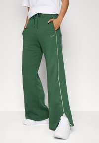 Gröna sweatpants i mjukt tyg, med avslappnad passform, vit sidostripe och dragsko i midjan. Svart logotyp på framsidan.