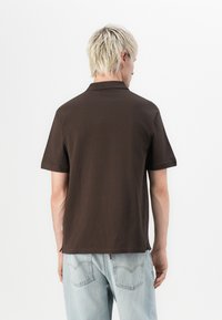 Bruine polo met korte mouwen en een klassieke kraag. Gemaakt van zachte stof, met een recht model en zijsplitten voor comfort.