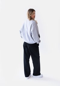 Szary, oversize'owy sweatshirt z opadłymi ramionami, w zestawieniu z czarnymi spódnicami o szerokich nogawkach i białymi sneakrsami. Minimalistyczny design na neutralnym tle.