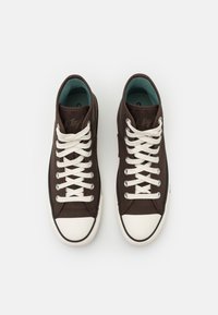 Bruna canvasneakers med vita skosnören, gummität på tån och ljusblått inre. Har sydd logotyp på sidan och vit sula.