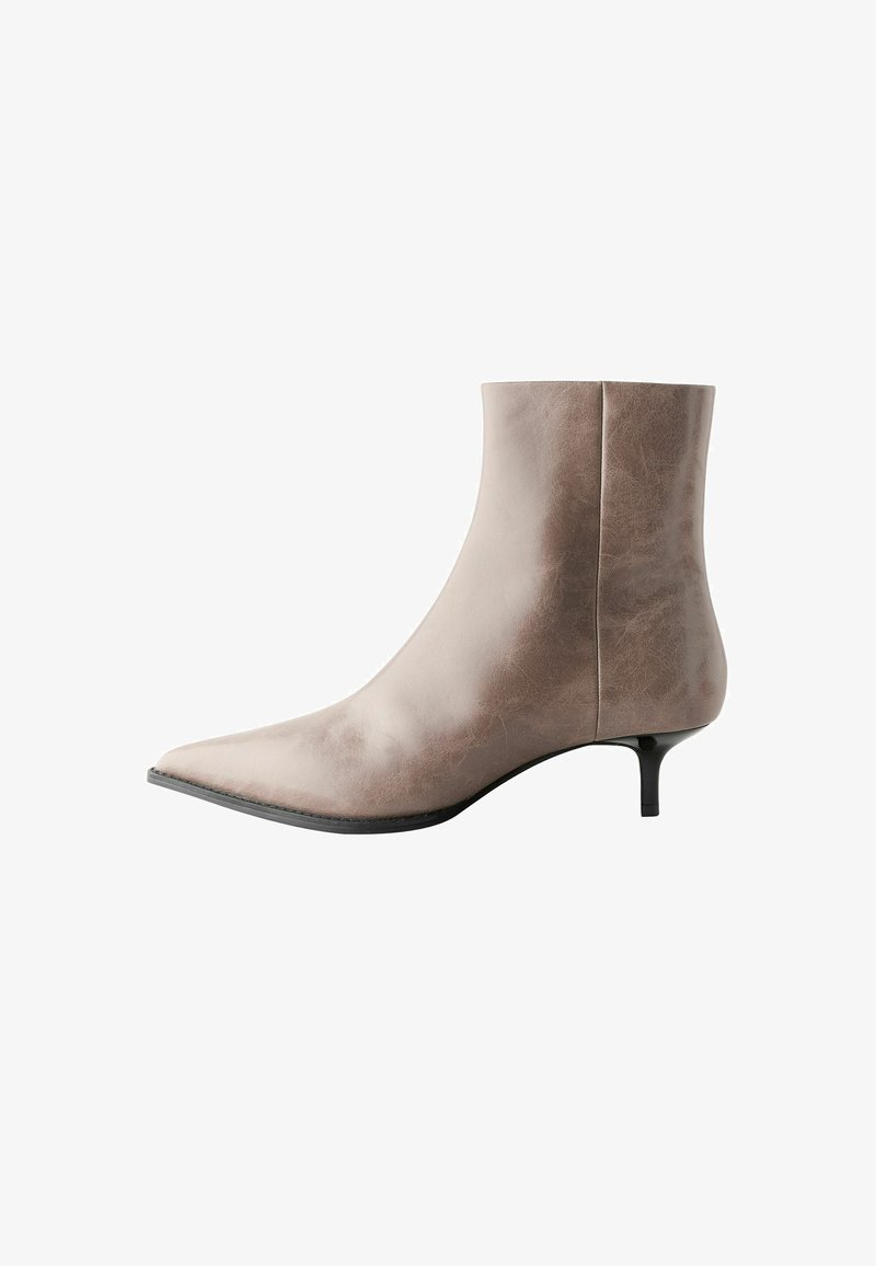 Botte en cuir marron à la cheville avec un bout pointu, un petit talon, une texture lisse et un design minimaliste, présentant une silhouette épurée sans ornements.