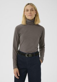 Graues langärmeliges Rollkragenhemd aus weichem Stoff, kombiniert mit dunkelblauen, hochgeschnittenen Hosen und einem schwarzen Gürtel mit silbernen Schnallenakzenten.
