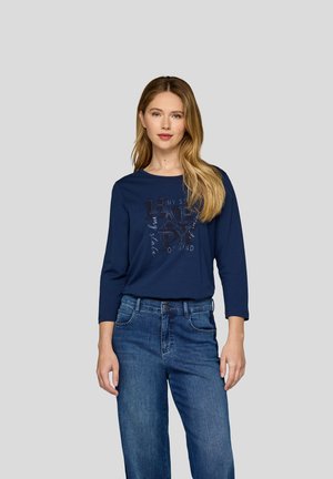 T-shirt à manches longues bleu marine avec impression de texte, associé à un jean bleu à lavage moyen. Matière en coton avec un bon ajustement et un col rond.