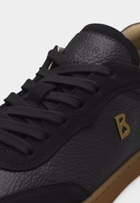 Μαύρο δερμάτινο αθλητικό παπούτσι με υφή, μαύρα κορδόνια, χρυσό λογότυπο "B" στο πλάι και καφέ λαστιχένια σόλα.