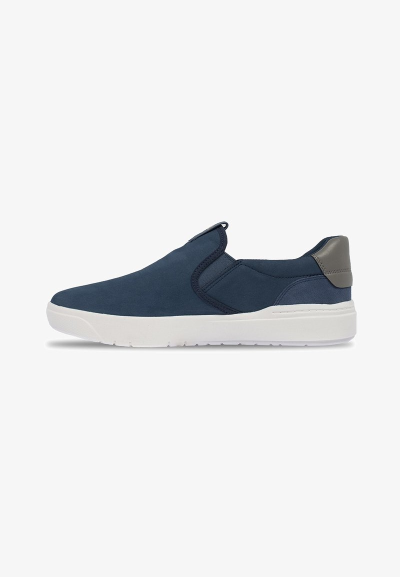Zapatos de ante azul marino sin cordones, con suela de goma blanca y un distintivo detalle en el talón gris, y paneles elásticos en los laterales para facilitar su uso.