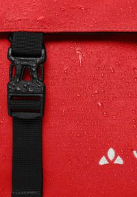 Borsa impermeabile rossa con una tracolla nera e fibbia. La superficie presenta gocce d'acqua e accenti di logo bianchi. Design in tessuto testurizzato.